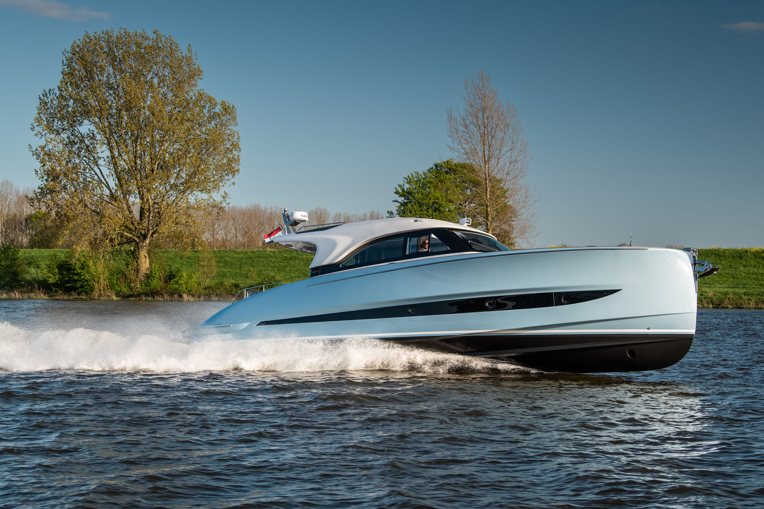 A sleek, modern yacht speeds across the water with a backdrop of trees and clear skies.