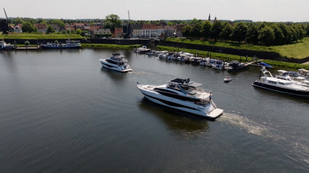 Luxe jachten van Princess Yachts varen in een schilderachtige haven met op de achtergrond een historische stad en een molen.