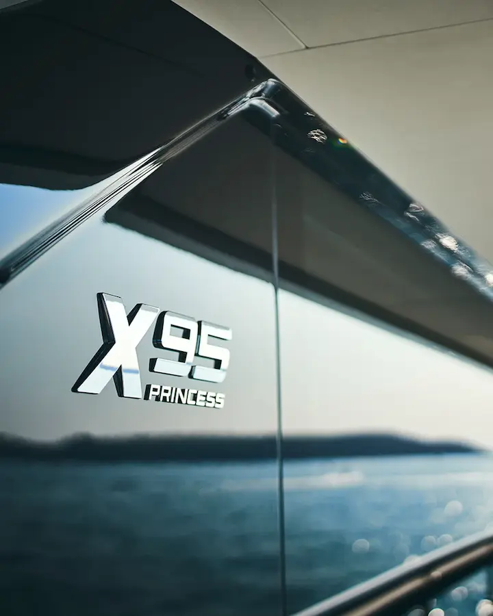 Close-up van het logo van de Princess Yachts X95 met zicht op de zee op de achtergrond.