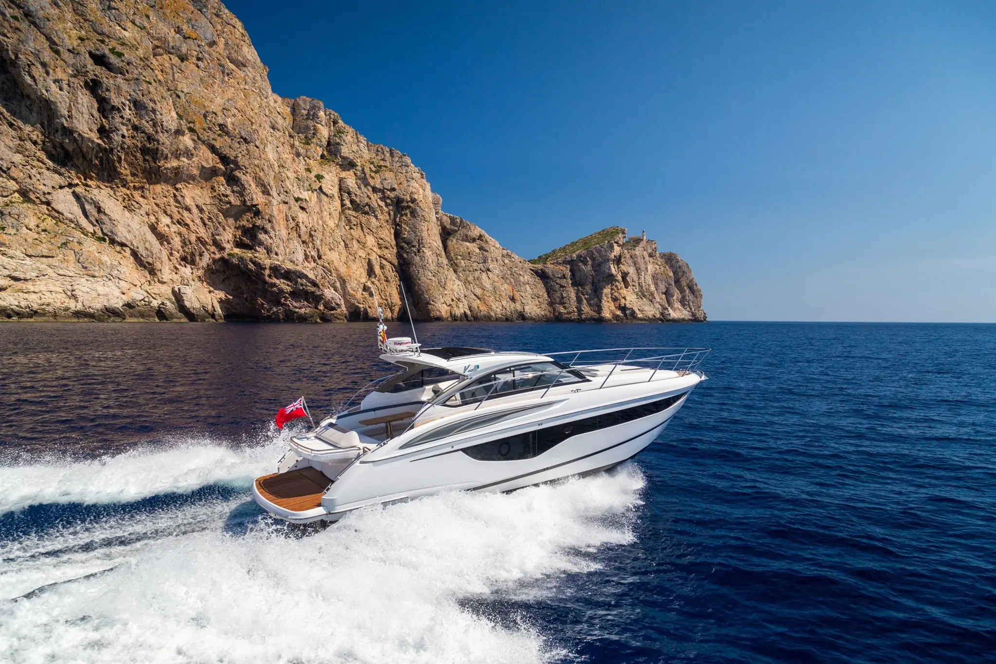 Een Princess Yachts V Class vaart langs indrukwekkende kliffen op een helderblauwe zee.