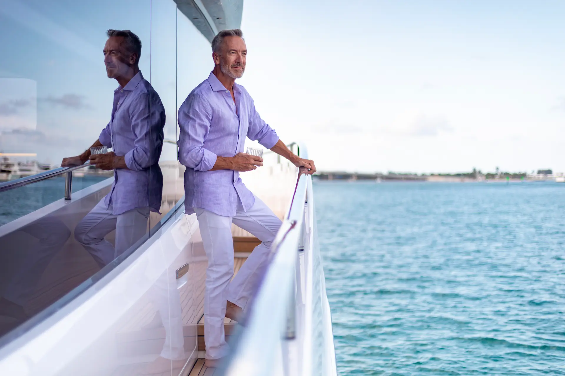 Man in een lichtpaarse blouse geniet van een drankje op het dek van een Princess Yachts boot met uitzicht op de zee.